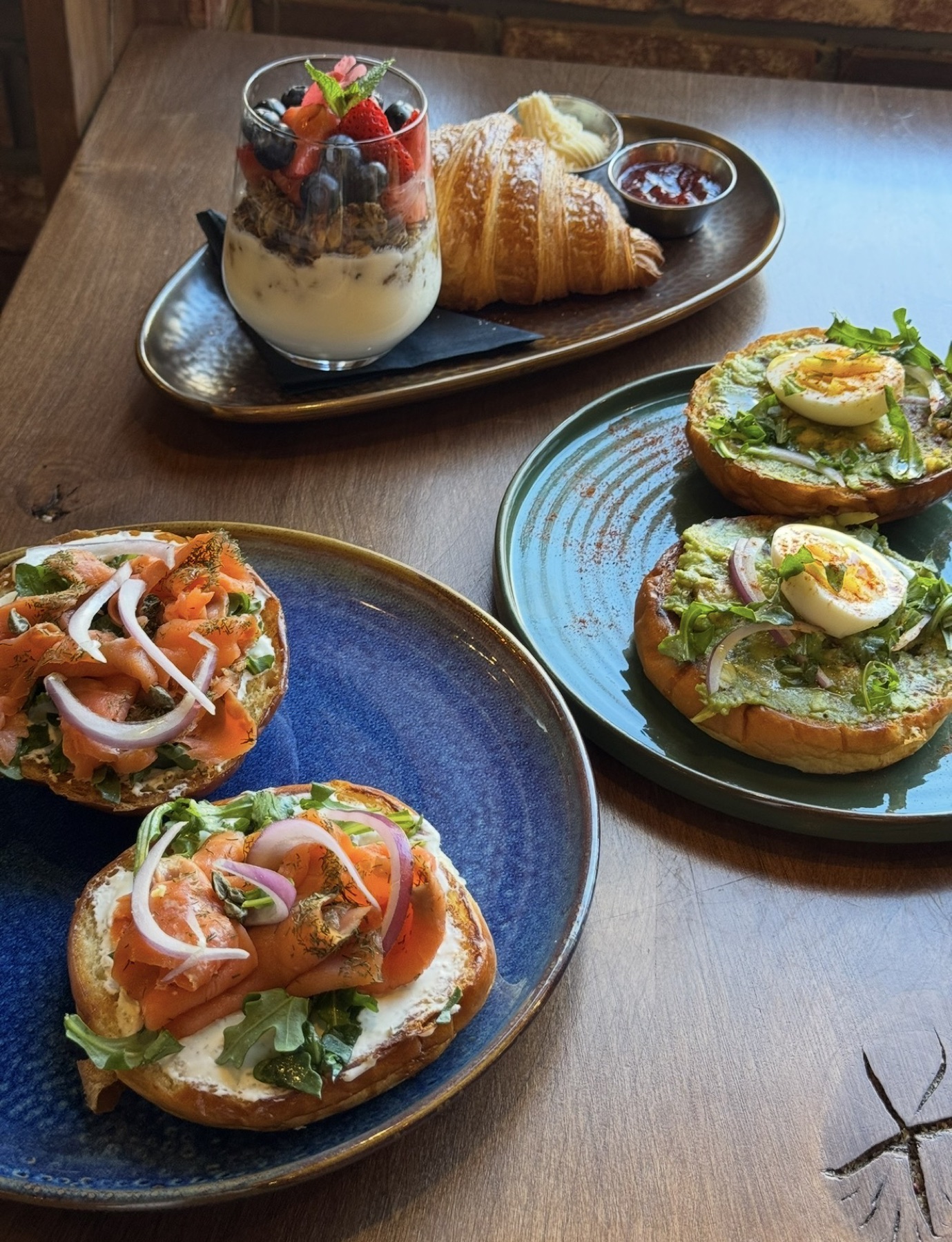 Brunch spread with smoked salmon bagels, avocado toast, croissant and a berry parfait