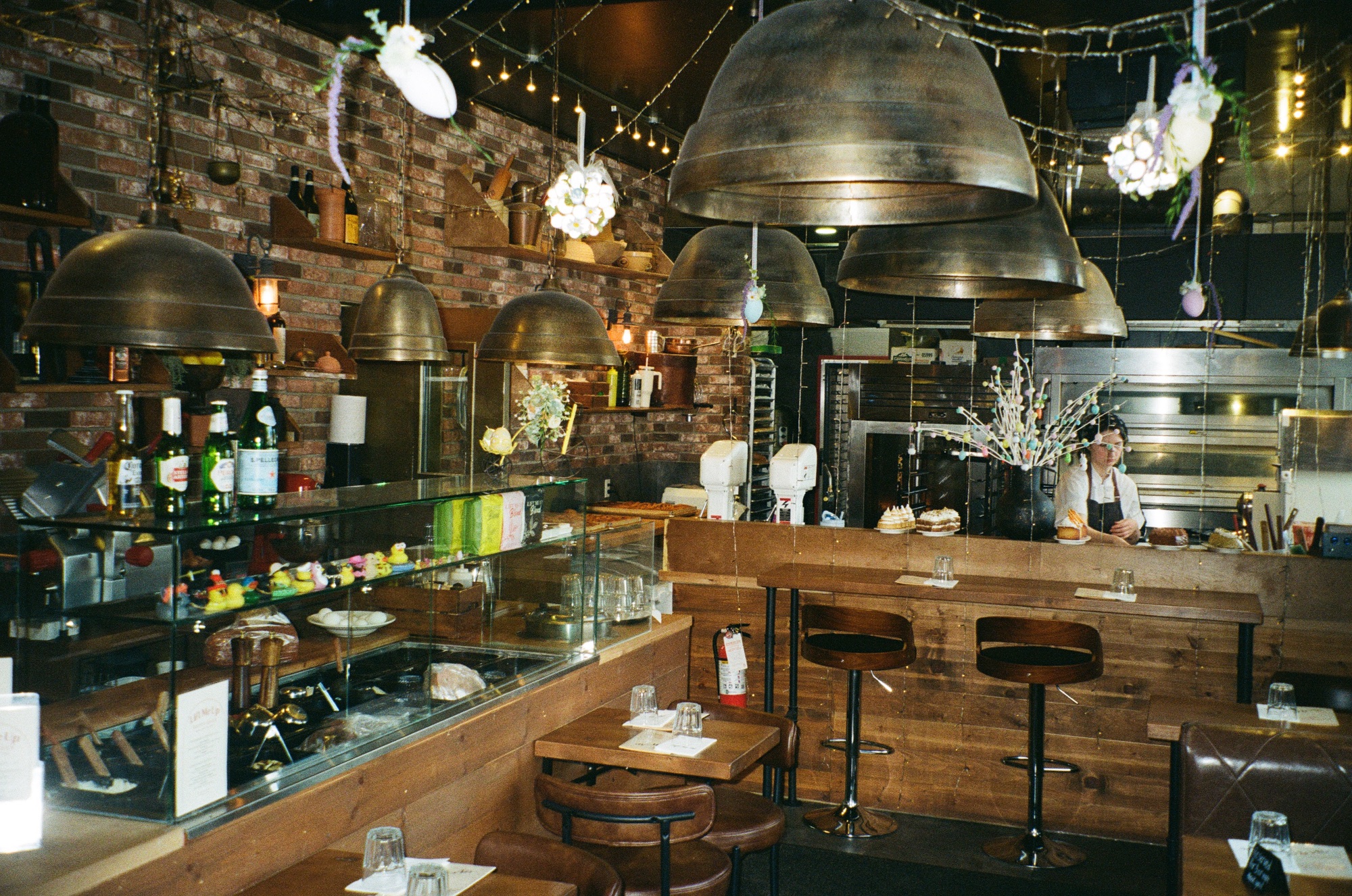 Interior with brass dome pendants, brick walls, the deli case and the bakery ovens behind the counter