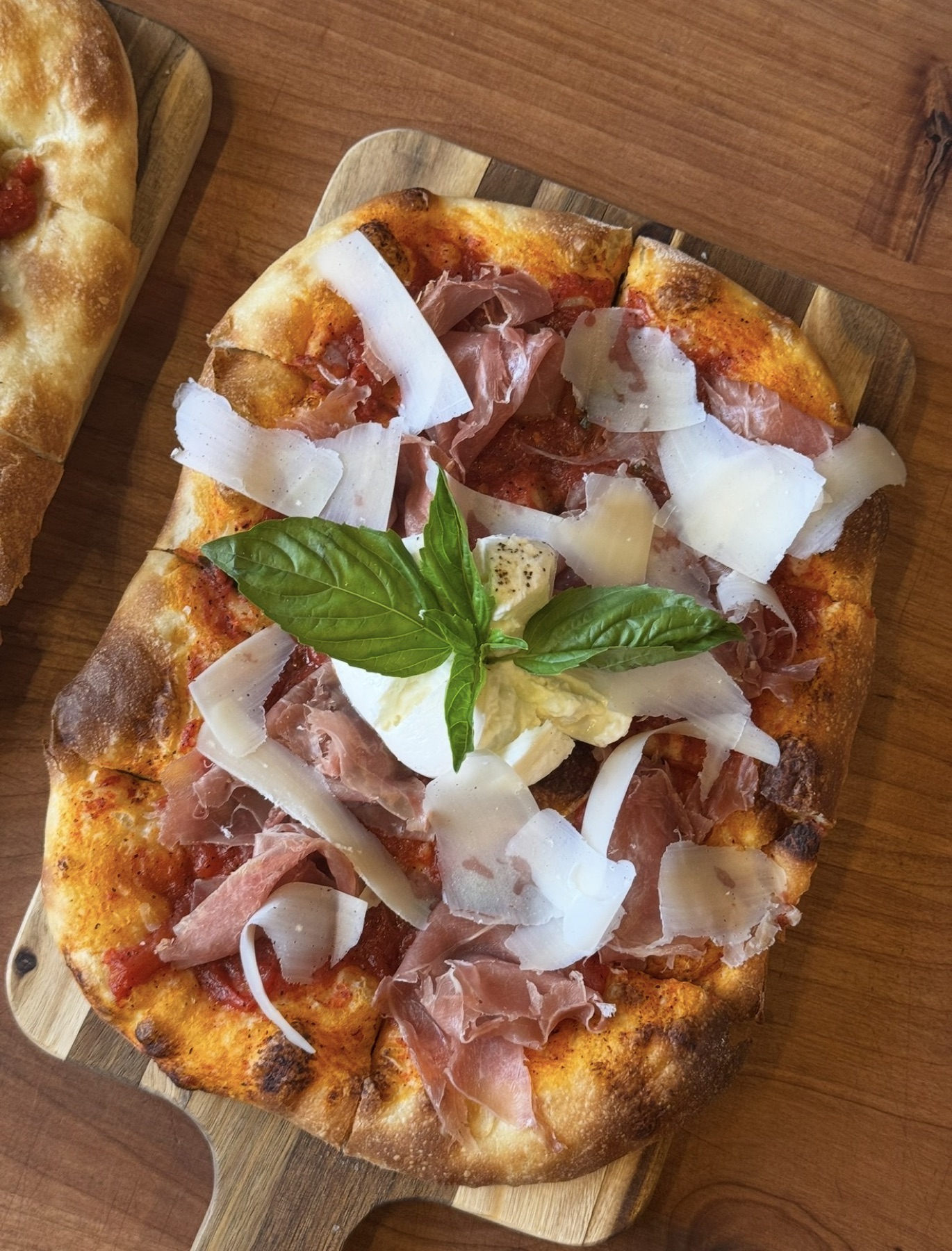 Prosciutto, burrata and shaved parmesan pizza on a wooden board